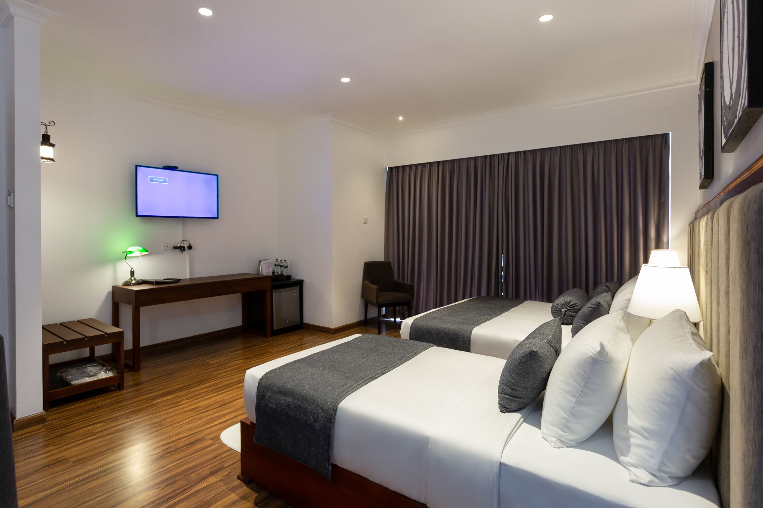 A hotel room with two beds, a desk, a television, and a chair.