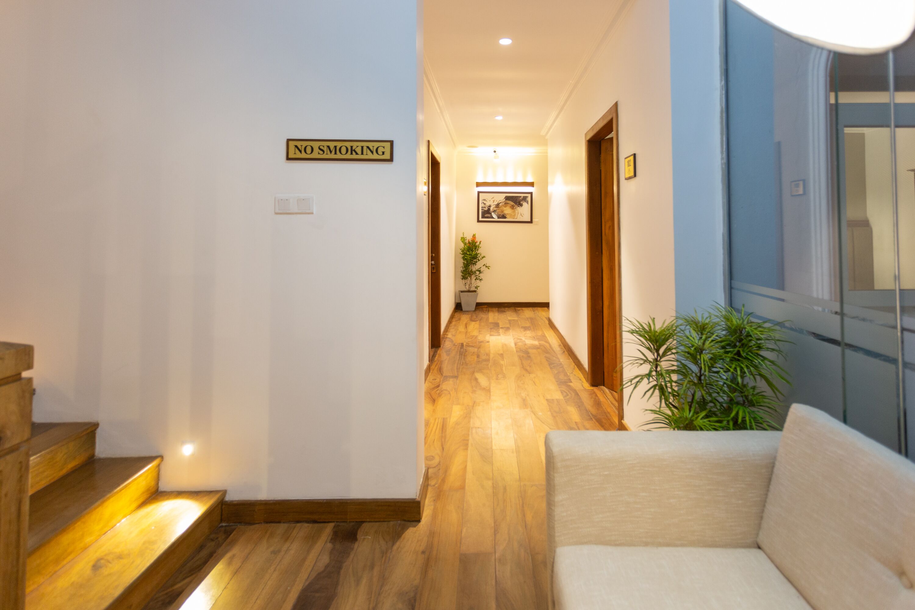 A hallway with a 'No Smoking' sign, wooden flooring, a sofa, and a potted plant.