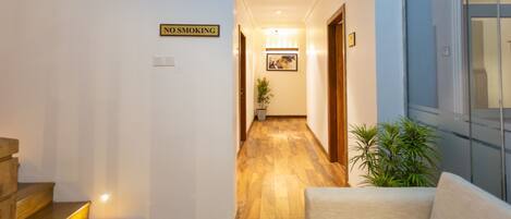 A hallway with a 'No Smoking' sign, wooden flooring, a sofa, and a potted plant.