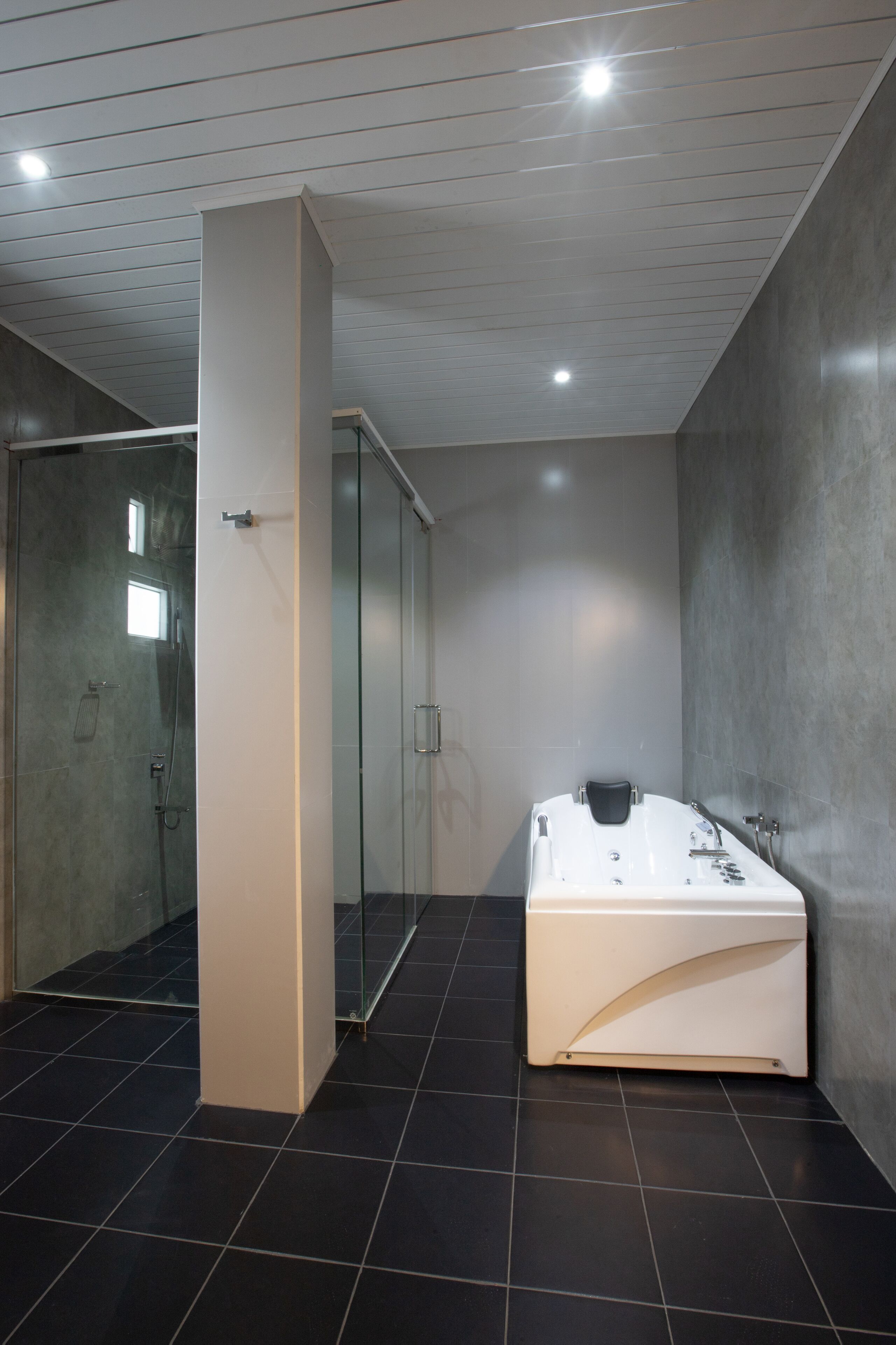 A modern bathroom with a glass-enclosed shower, a white bathtub, and dark tiled flooring.