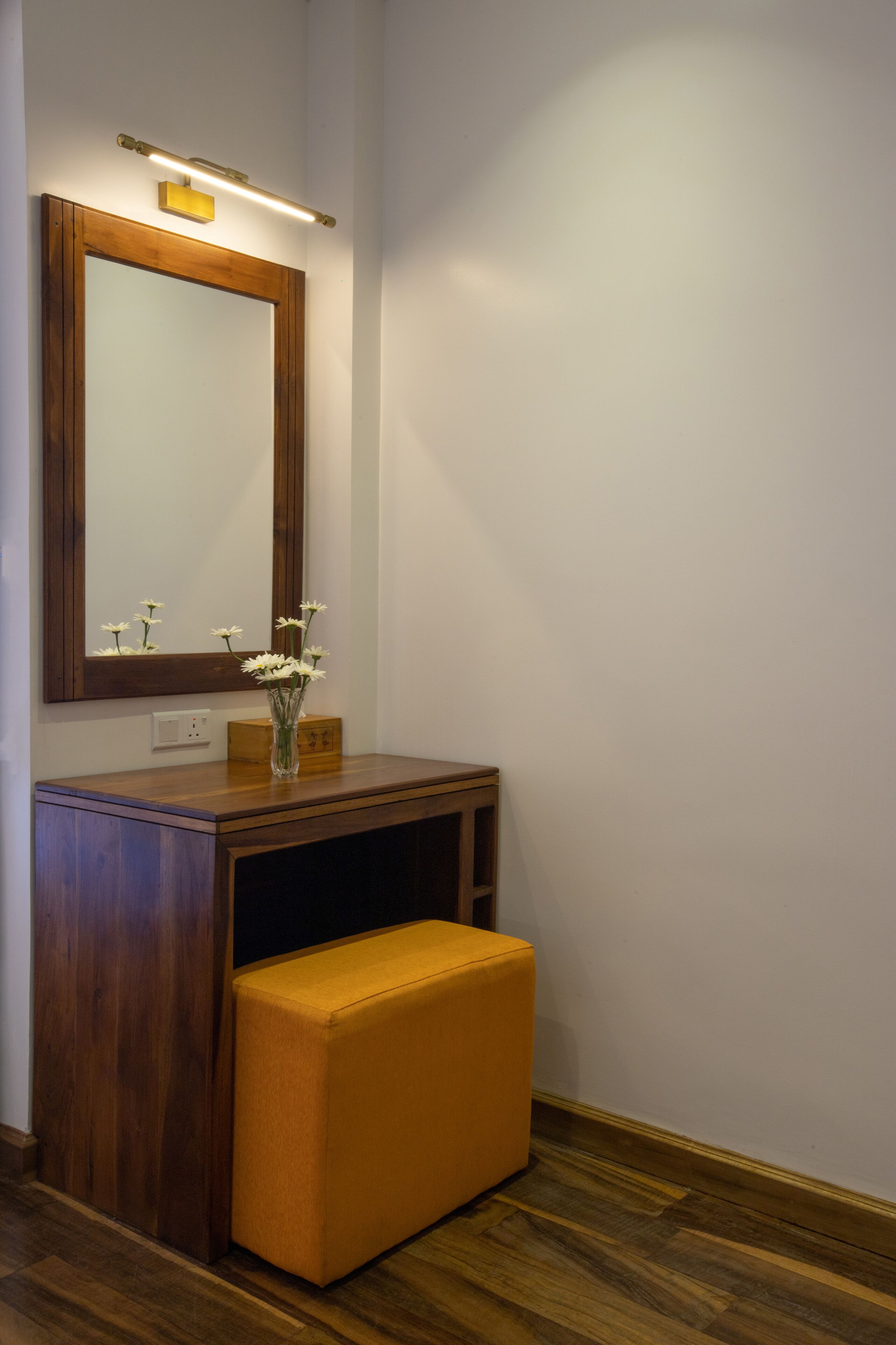 A wooden vanity with a mirror, a vase with flowers, and a bench.