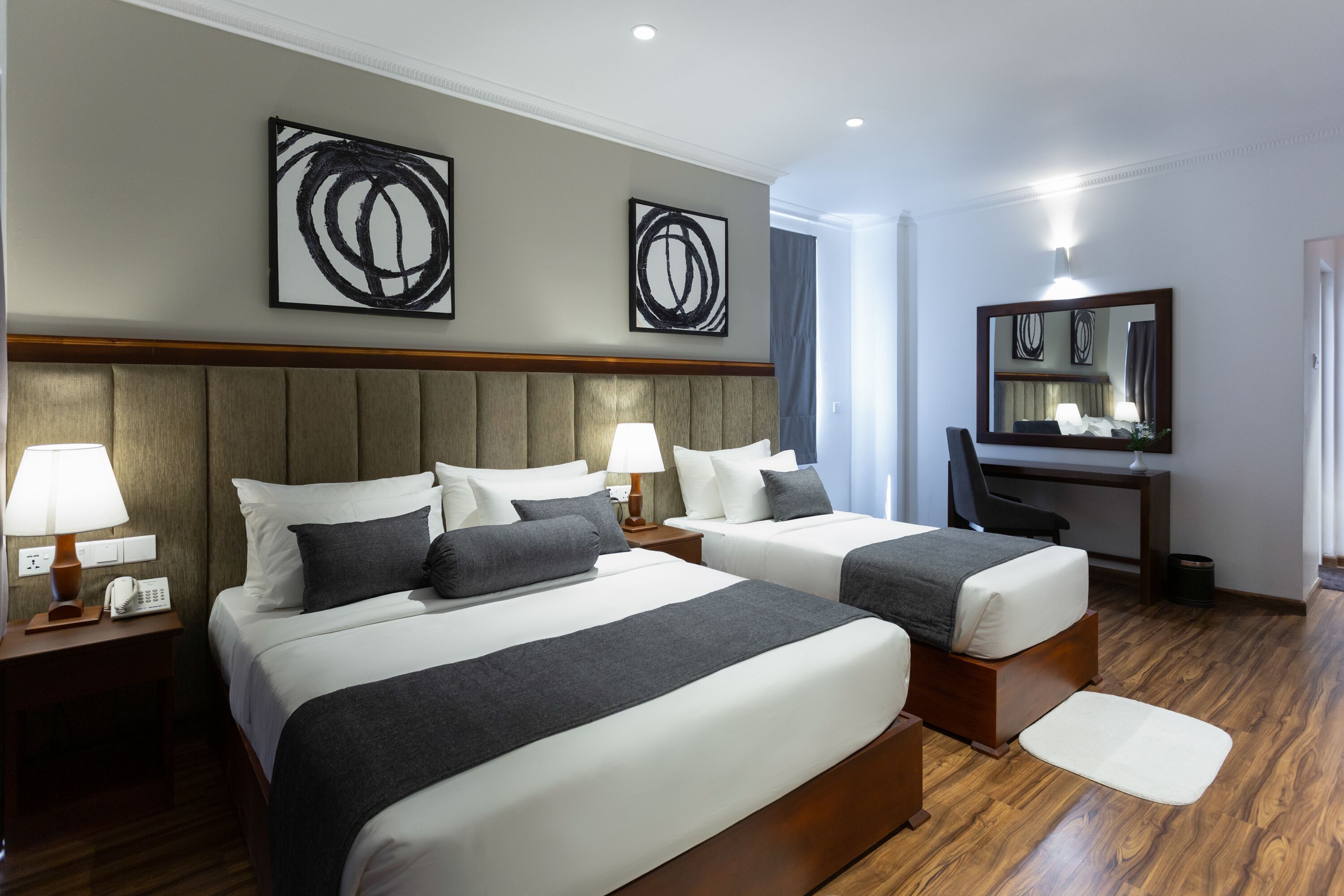 Habitación de hotel con dos camas, un escritorio, una silla y obras de arte en las paredes.