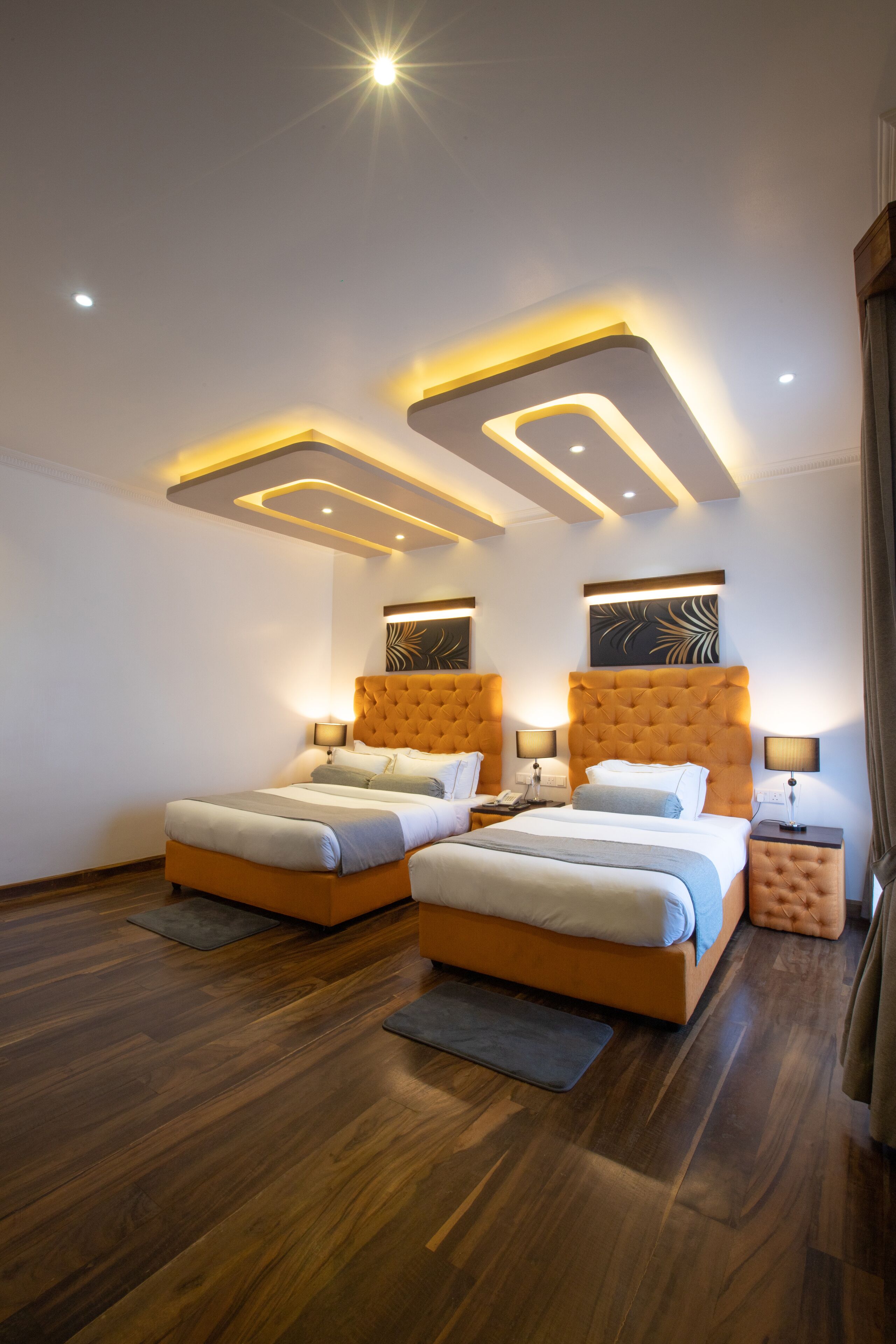 A modern bedroom with two beds, wooden flooring, and recessed ceiling lighting.