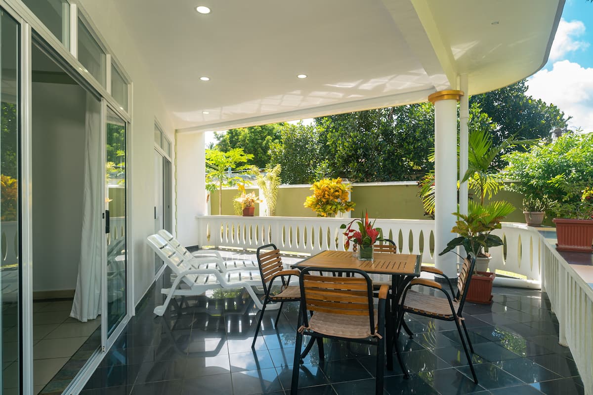 A covered patio with a table and chairs, potted plants, and a view of greenery.