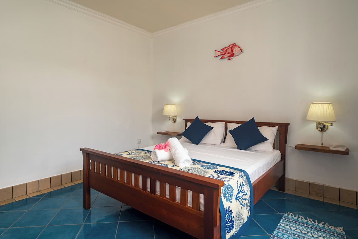 A neatly made bed with a blue and white patterned bedspread, two pillows, and a rolled towel on the bed. There are two wall-mounted lamps on either side of the bed.