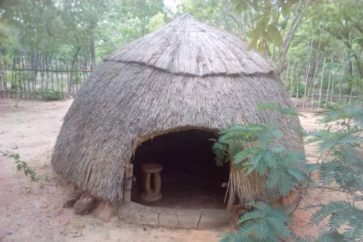 Eine reetgedeckte Hütte mit offenem Eingang und einem Hocker darin.