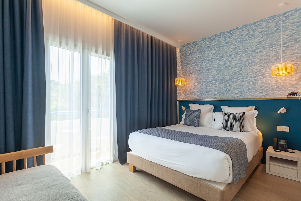 Een net opgemaakt bed met een wit en grijs dekbed, een houten hoofdbord en een nachtkastje met een lamp.