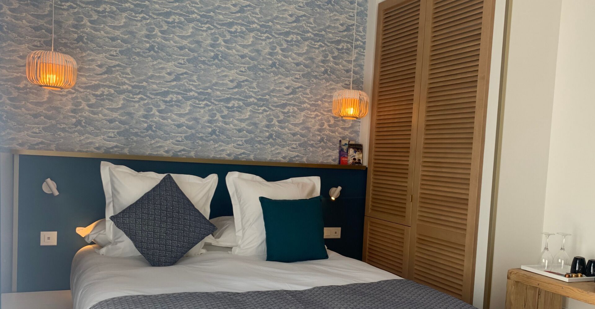 Ein ordentlich bezogenes Bett mit weißen und türkisfarbenen Kissen, einem blauen Kopfteil und einer strukturierten Wand dahinter.