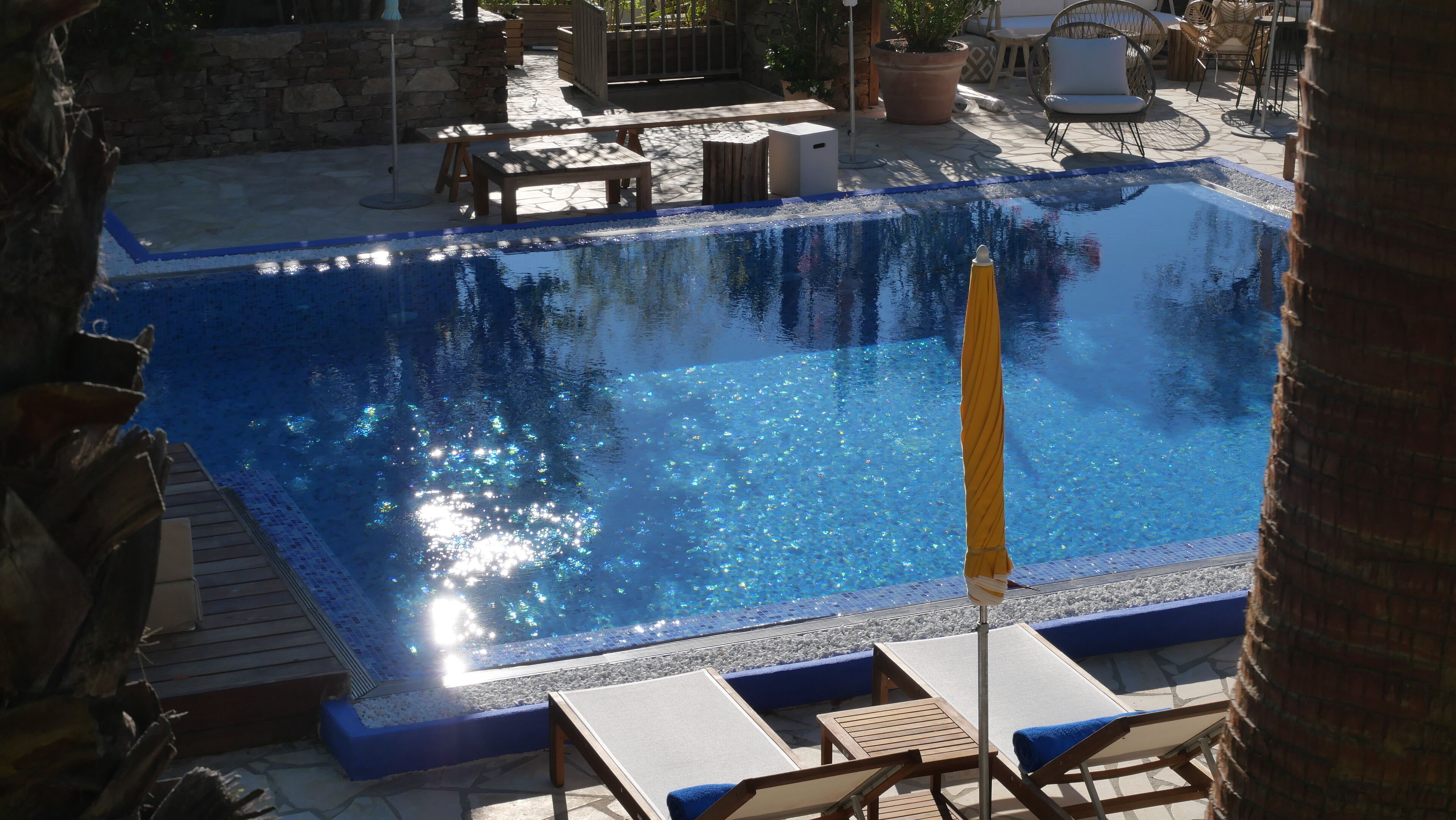 A swimming pool with lounge chairs and a stone wall in the background.