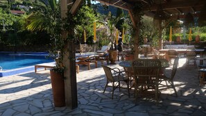 Un espace aménagé au bord de la piscine, avec des chaises longues, une table et une pergola décorée de guirlandes lumineuses.