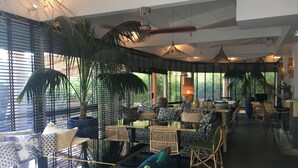 Un espace de restauration intérieur moderne, doté de tables et de chaises, de grandes fenêtres et de plantes en pot.