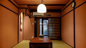 A traditional Japanese room with tatami flooring, a wooden table, a hanging light fixture, and a sliding door. - Nishioji Tanuki (Kyoto)