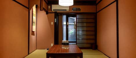A traditional Japanese room with tatami flooring, a wooden table, a hanging light fixture, and a sliding door.
