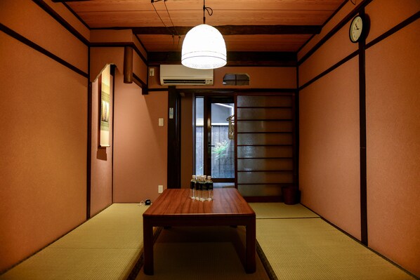 A traditional Japanese room with tatami flooring, a wooden table, a hanging light fixture, and a sliding door.