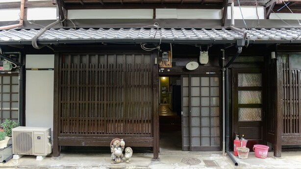 A traditional Japanese building with a tiled roof, a wooden entrance gate, and a small air conditioning unit outside. - Nishioji Tanuki (Kyoto)