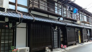 A traditional Japanese building with a tiled roof, wooden balconies, and a small shrine figure on the ground floor. - Nishioji Tanuki (Kyoto)