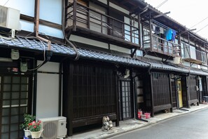 Un edificio japonés tradicional con tejado de tejas, balcones de madera y una pequeña figura de santuario en la planta baja.