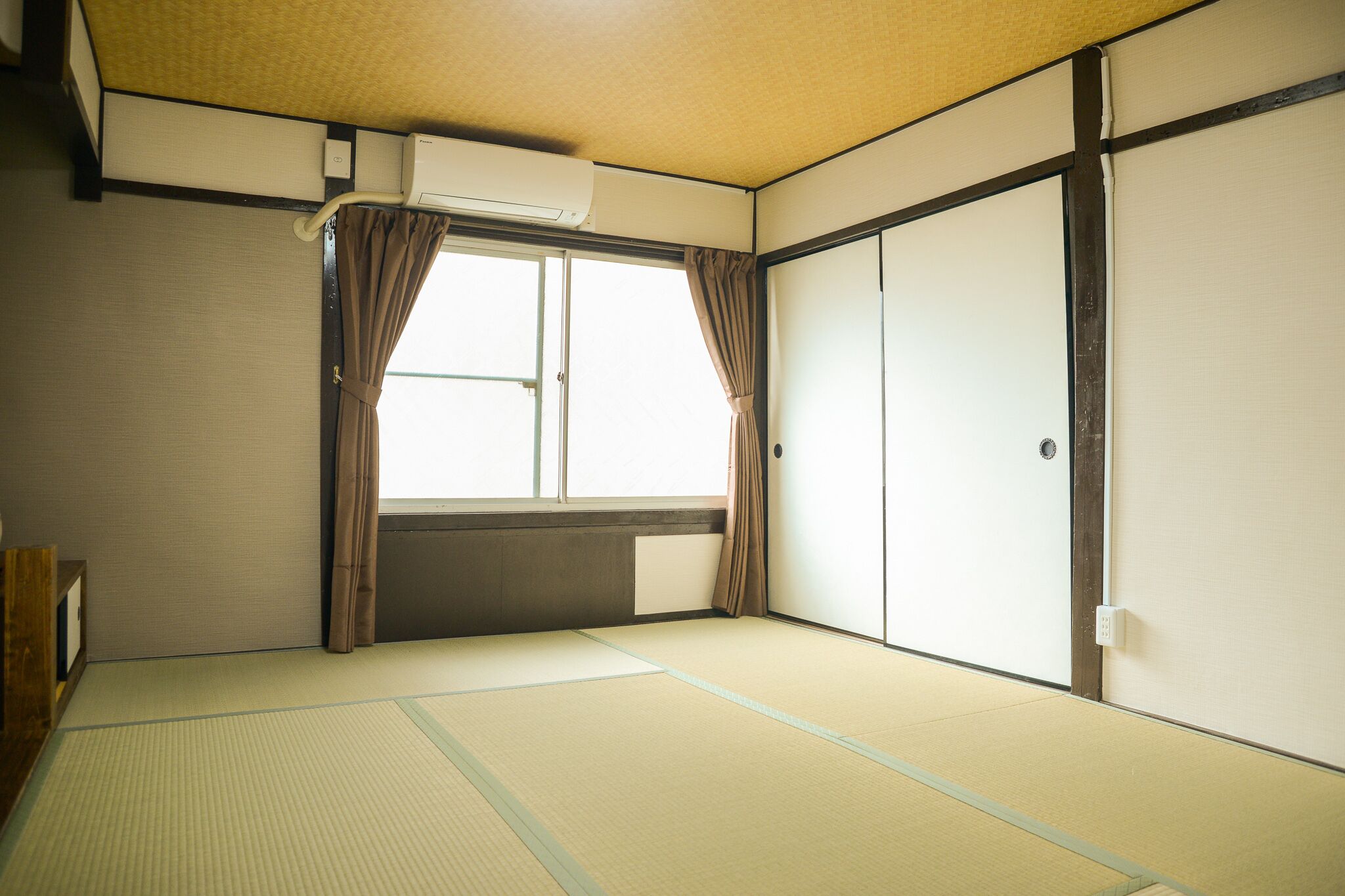Ein traditioneller japanischer Raum mit Tatami-Boden, Schiebetüren und einem Fenster mit Vorhängen.