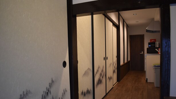 A hallway with sliding doors featuring traditional artwork, a wooden floor, and a kitchen area with appliances. - Nishioji Fukuro (Kyoto)