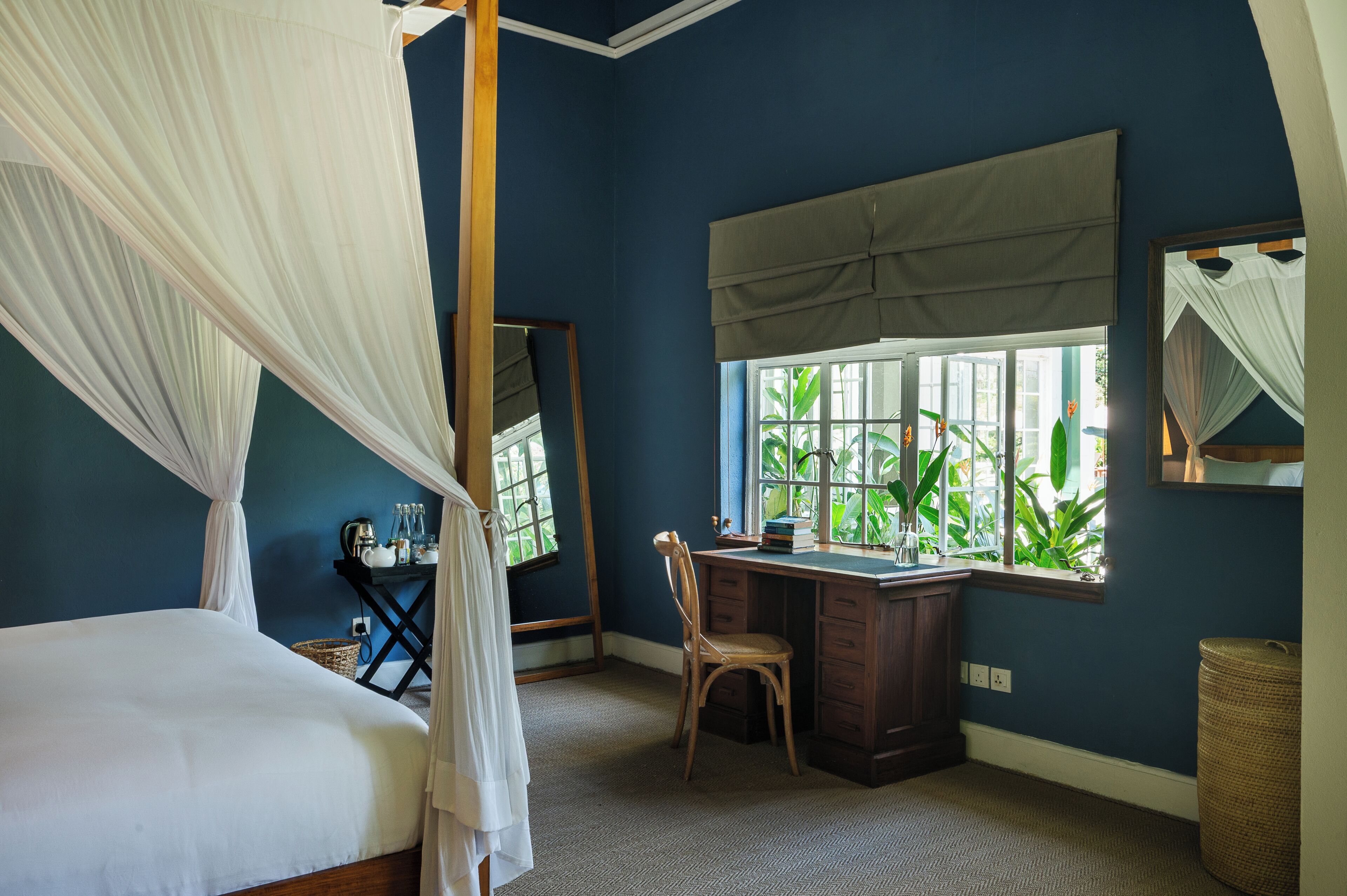 Quarto com cama de dossel, escrivaninha e janela com vista para o verde.