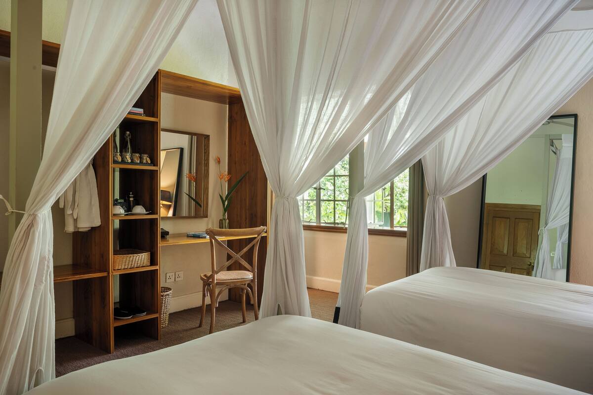 A bedroom with a canopy bed, a wooden bookshelf, a chair, and a mirror.