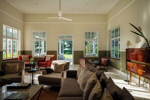 A spacious living room with multiple seating areas, large windows, and a ceiling fan.