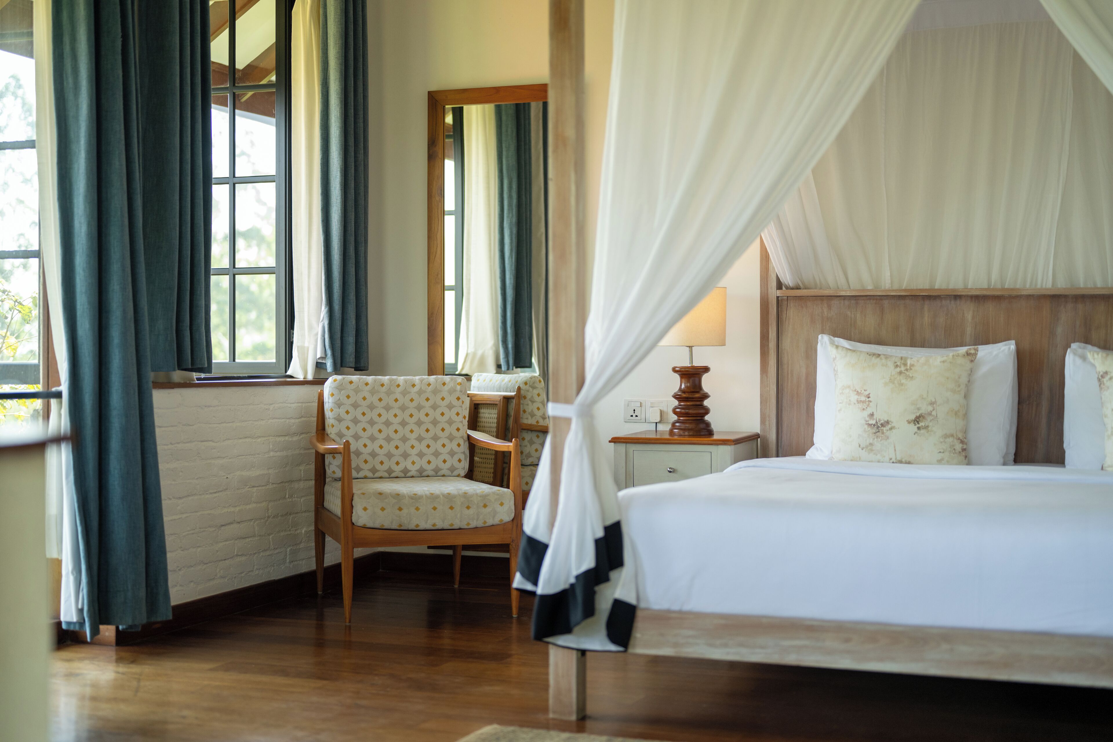 A bedroom with a wooden bed, a chair, a bedside table, and a window with curtains.