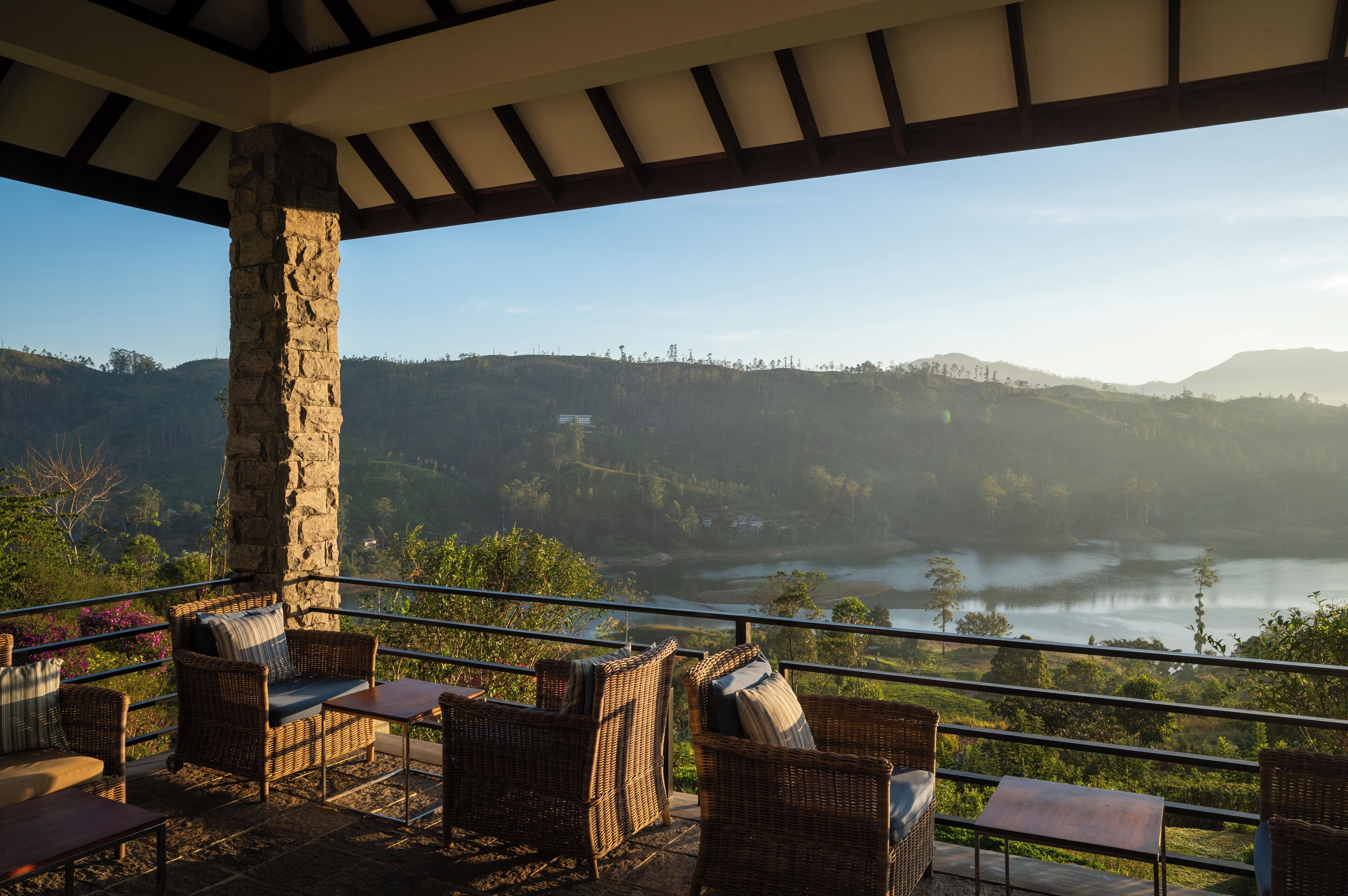 Una terraza con muebles de mimbre y un pilar de piedra, con vistas a un valle y un lago.