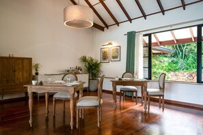 A dining area with wooden furniture, a hanging light fixture, and a view of greenery outside. - Camellia Hills (Hatton)