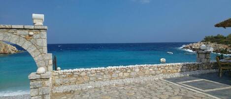A stone pathway leading to a stone wall overlooking a clear blue sea.