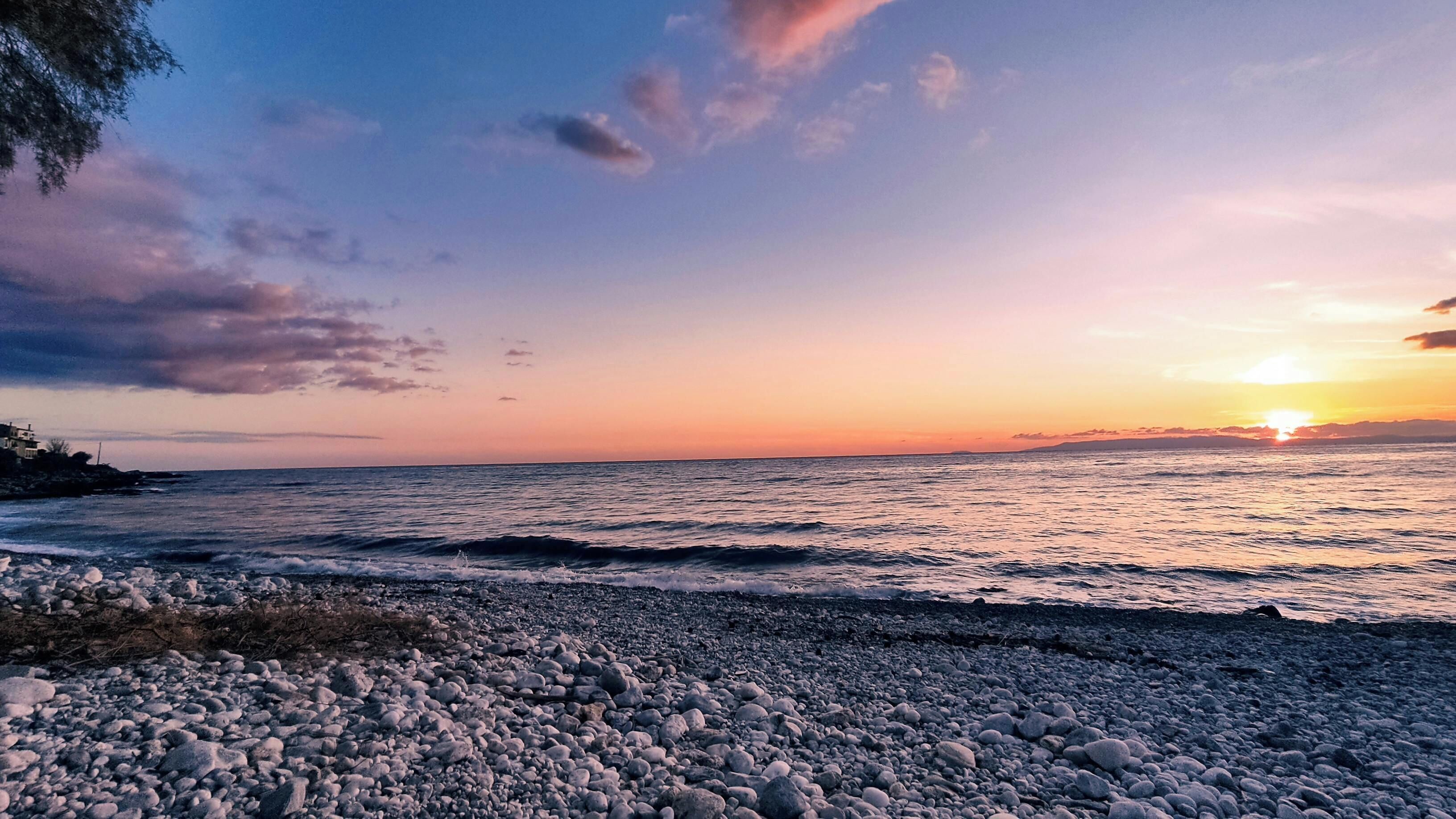 Una playa con piedras y un atardecer sobre el agua.