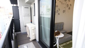 A small balcony with a sliding glass door, a white radiator, a grey sofa, and a small table with a cat. - Hotel Central Yokohama (Yokohama)