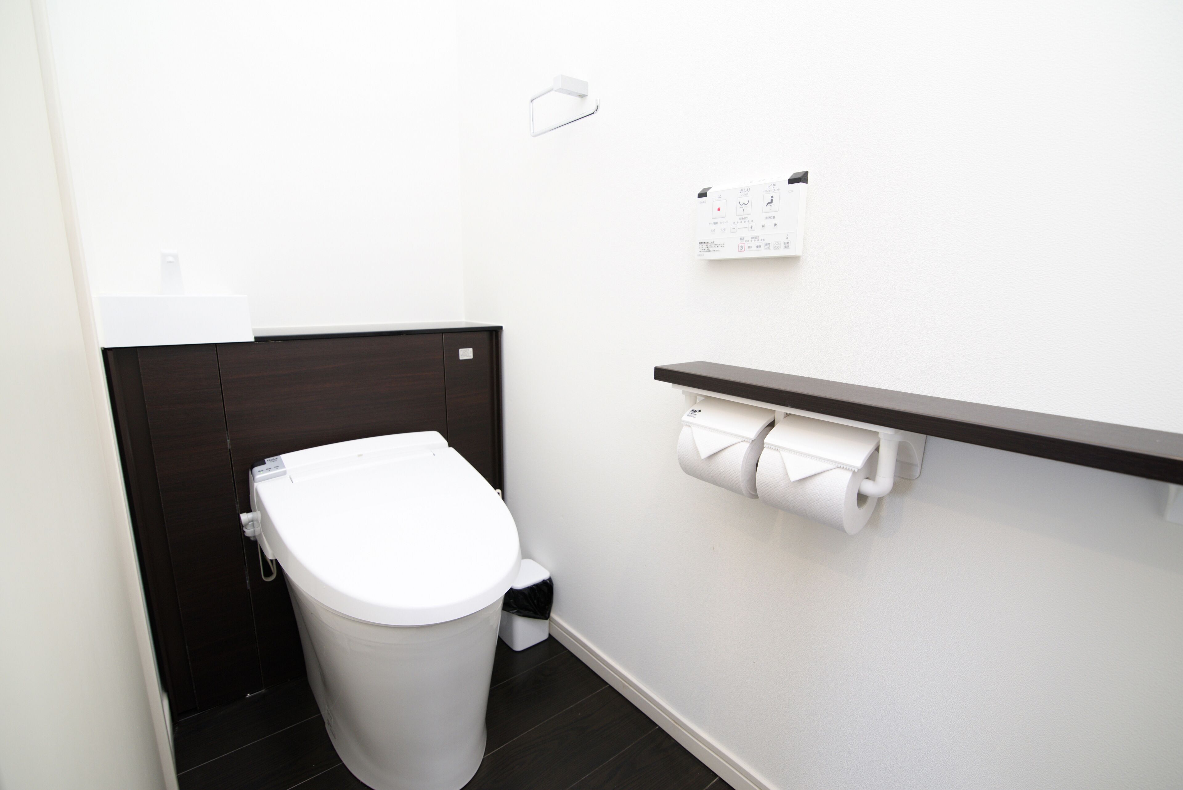 Ein modernes Badezimmer mit Toilette in Weiß, dunklen Holzvertäfelungen, einem weißen Waschbecken und einem Toilettenpapierhalter an der Wand.