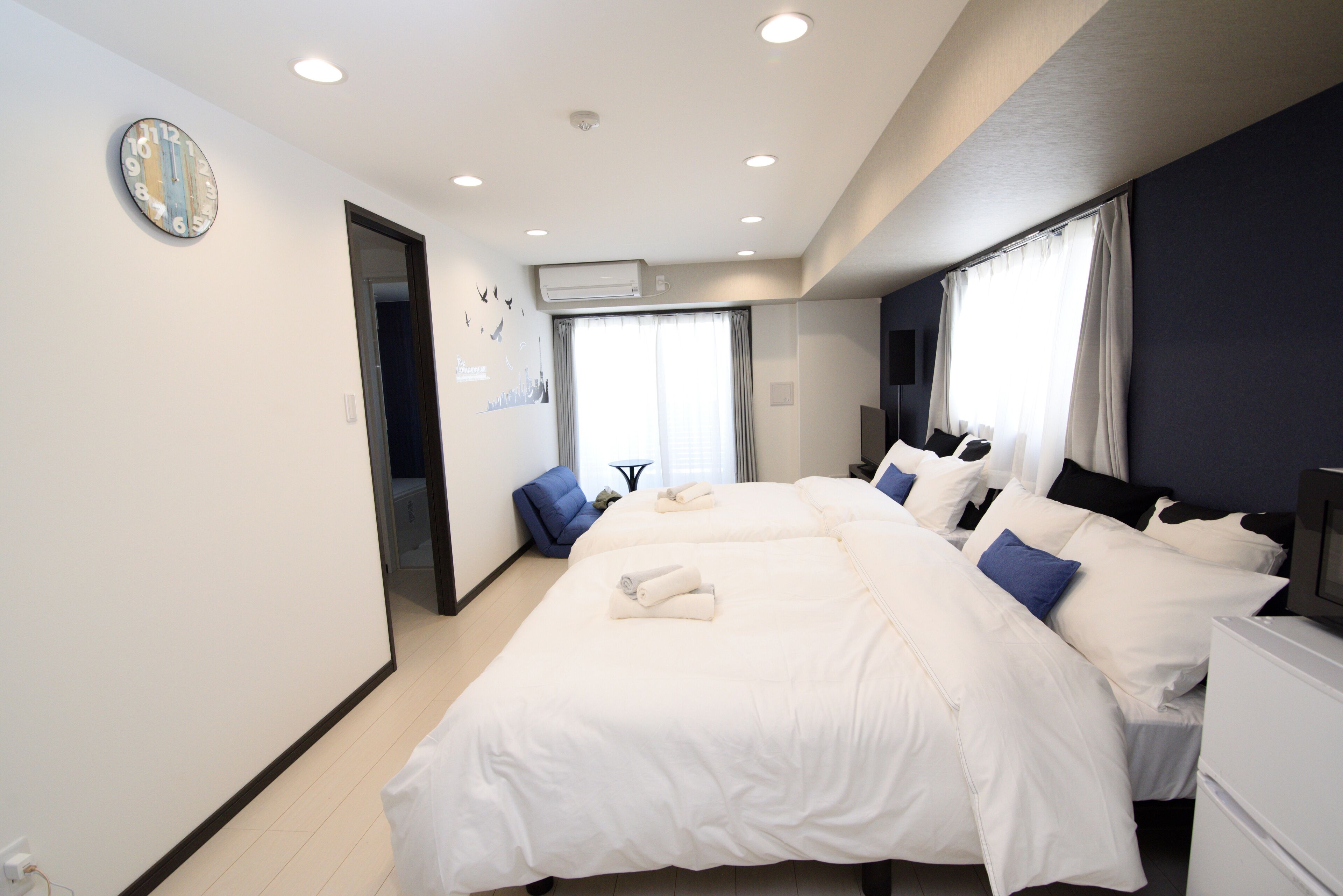 A hotel room with two beds, a large wall clock, and an air conditioning unit.