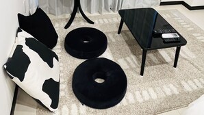 A modern living room with a sofa, two black round ottomans, a small black side table, and a black coffee table with a remote control. - Hotel Central Yokohama (Yokohama)