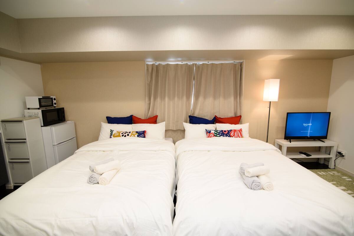 Ein Hotelzimmer mit zwei Betten, einem Fernseher, einem Schreibtisch und einer Mikrowelle.