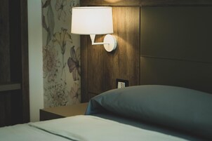 Habitación de hotel con una cama, una mesita de noche, una lámpara de pared y un estampado de papel tapiz floral.