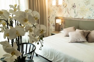 Una camera d'albergo con un letto, un comodino con una lampada, una sedia e carta da parati con motivi floreali.
