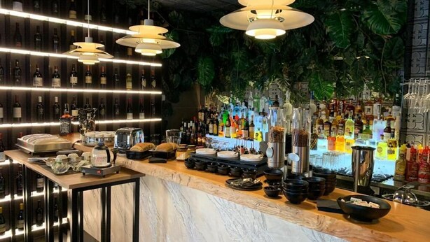 A bar area with a marble countertop, hanging pendant lights, and a variety of bottles and glasses. - Hotel Pontemare (Palermo)