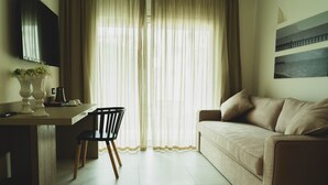 A modern living room with a sofa, a dining table with chairs, and a TV mounted on the wall. - Hotel Pontemare (Palermo)