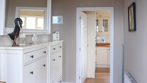 A hallway with a white dresser, a black sculpture, and a door leading to a kitchen. - Atlantic Rose Cottage (Lisdoonvarna)