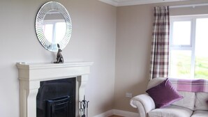 A living room with a fireplace, a sofa, and a window with curtains. - Atlantic Rose Cottage (Lisdoonvarna)