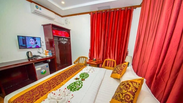 A hotel room with a bed, a desk, a television, and red curtains. - True Treasure Hotel (Taunggyi)