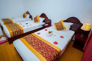 Two single beds with white and gold bedspreads, red floral pillows, and a red nightstand with a lamp. - True Treasure Hotel (Taunggyi)