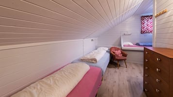 A dormitory room with two single beds, a wooden dresser, and a small desk with a chair.