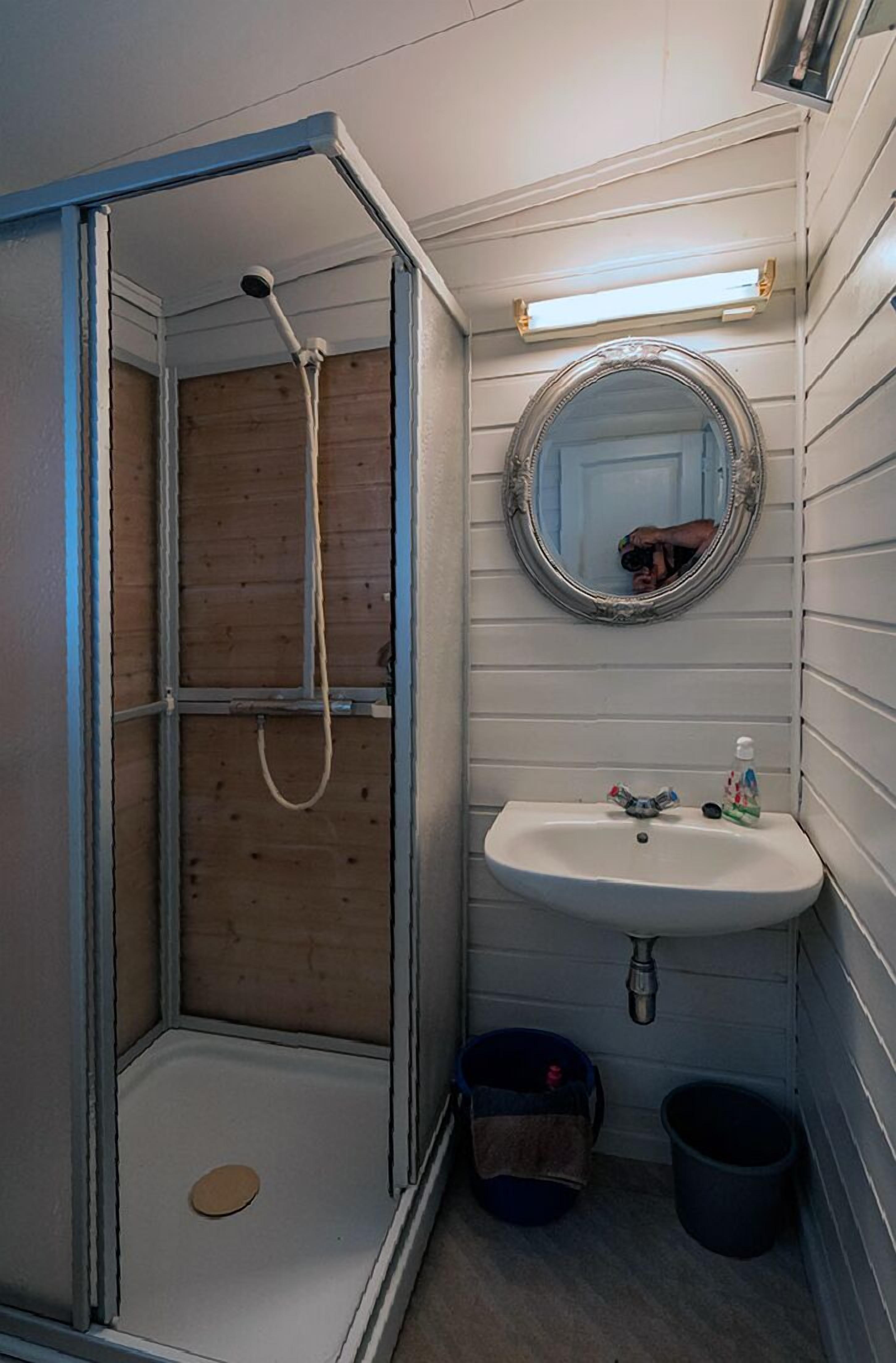 A small bathroom with a shower, a sink, a mirror, and a light fixture.