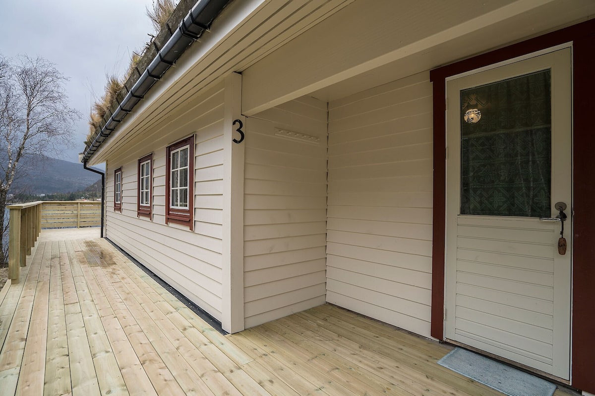 A wooden deck with a house number 3, a door with a decorative glass panel, and a view of mountains in the background.
