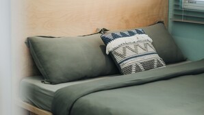 Una cama con ropa de cama verde y un cojín decorativo estampado.
