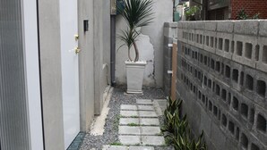 Un callejón estrecho con un sendero de concreto, plantas en macetas y un muro de ladrillo.