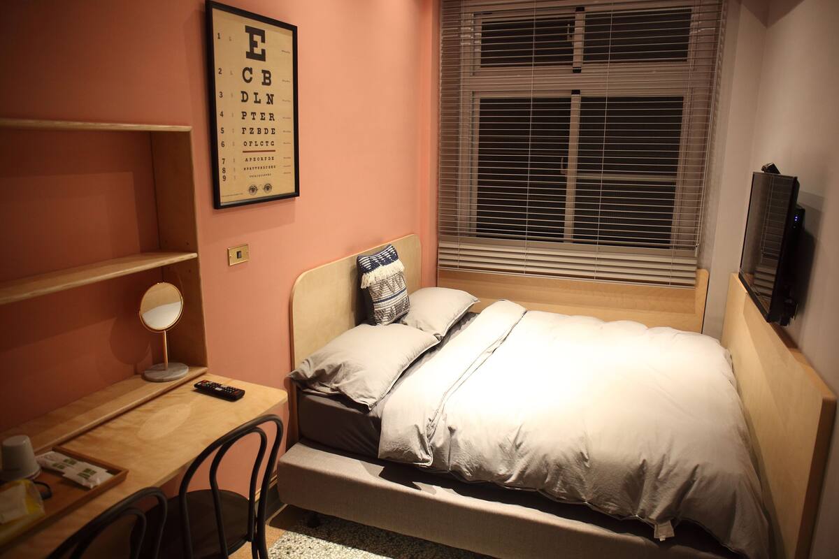 Un dormitorio con cama, escritorio con silla, espejo y ventana con persianas.